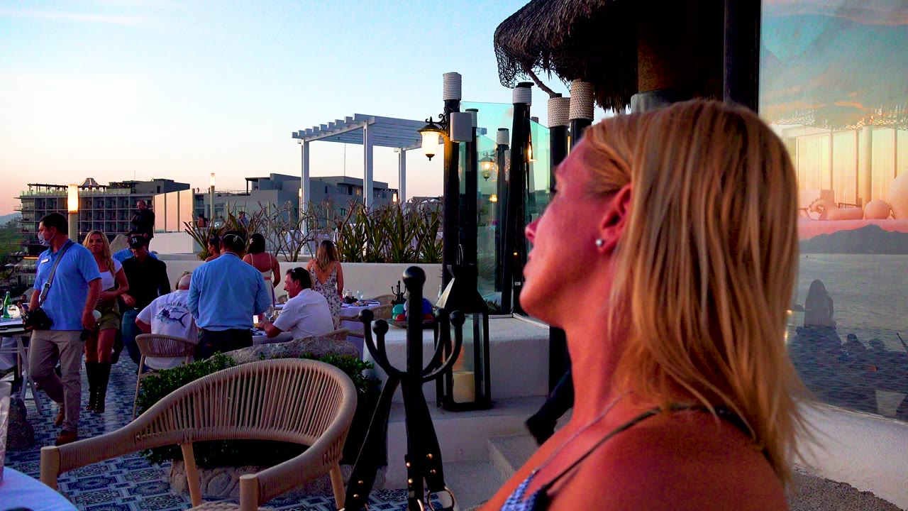 Foreground woman looking left toward people gathered on a terrace