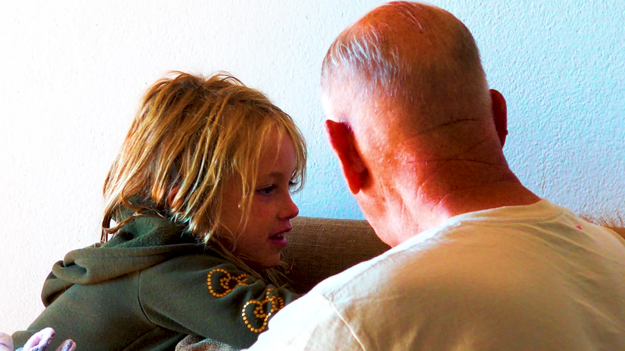 Child looks toward an adult man while seated on a couch.