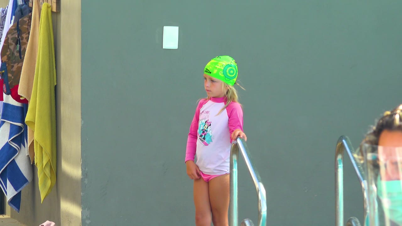 Girl in swim cap standing beside the pool handrail.