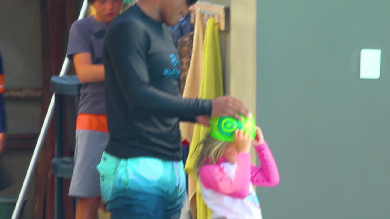 Adult and child are partly blurred while adjusting a green swim cap.