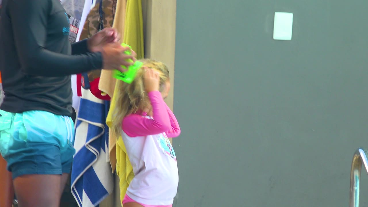 Adult holding a bright green item over a blonde child's hair.