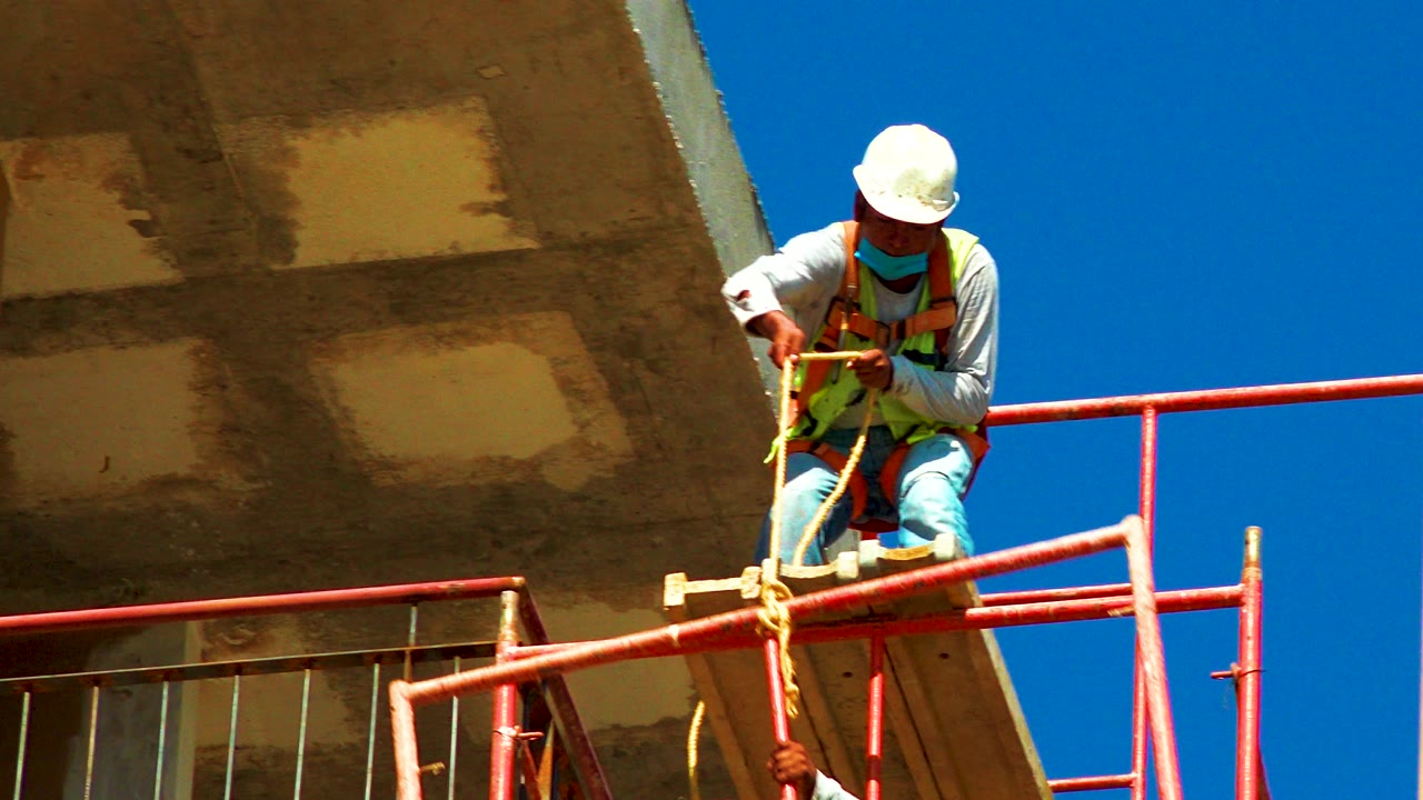 Worker in safety gear handling orange pipe on a scaffold.