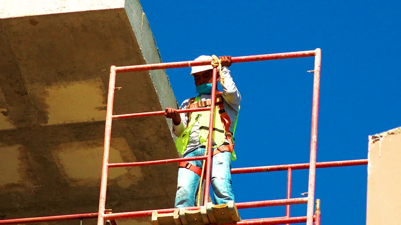 Worker stands behind a red railing near a concrete overhang.