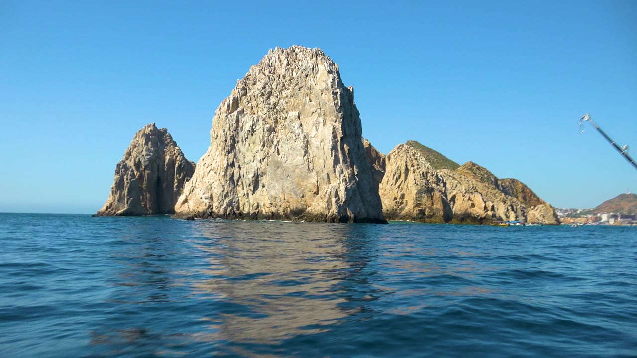 Cabo San Lucas rock formations stand beyond rippled blue water at the start of the clip, with clear sky above and no visible people.