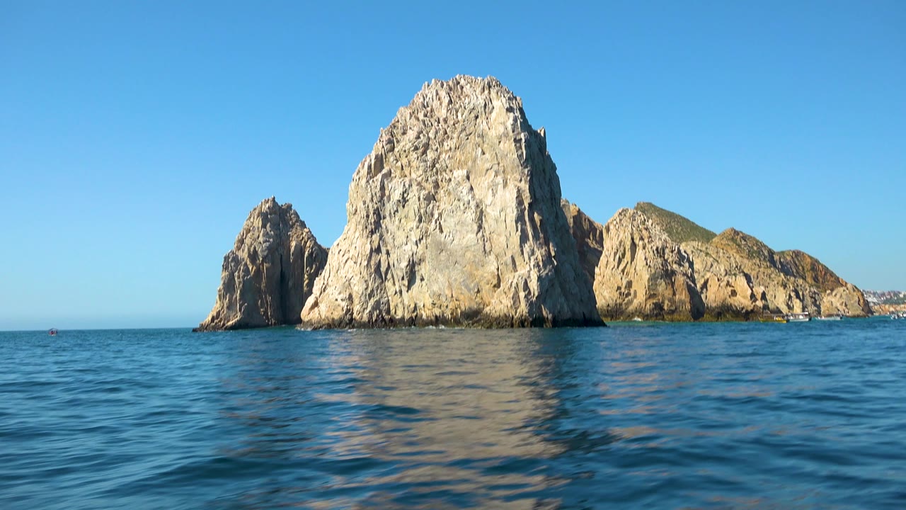 Cabo San Lucas rock formations sit centered across the ocean, with open water in front, a low shoreline to the right, and no visible people.