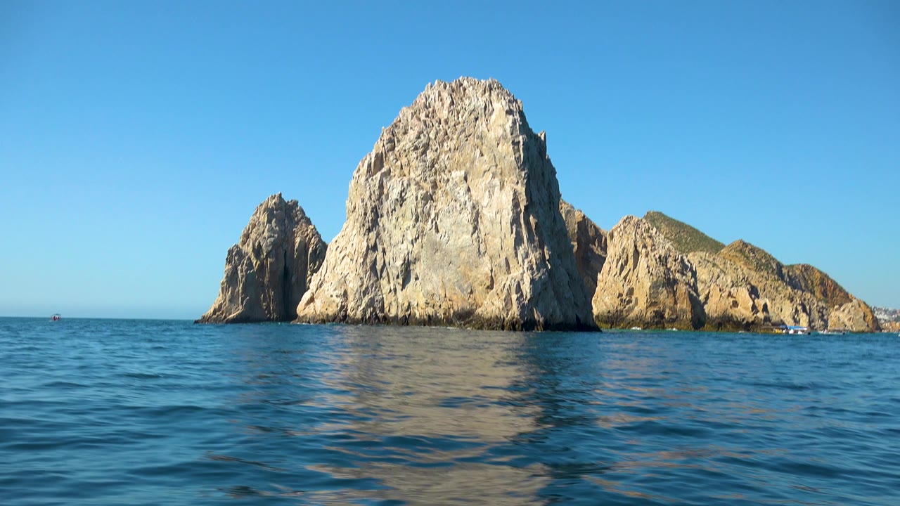 Large sea rocks reflected in rippled blue water.