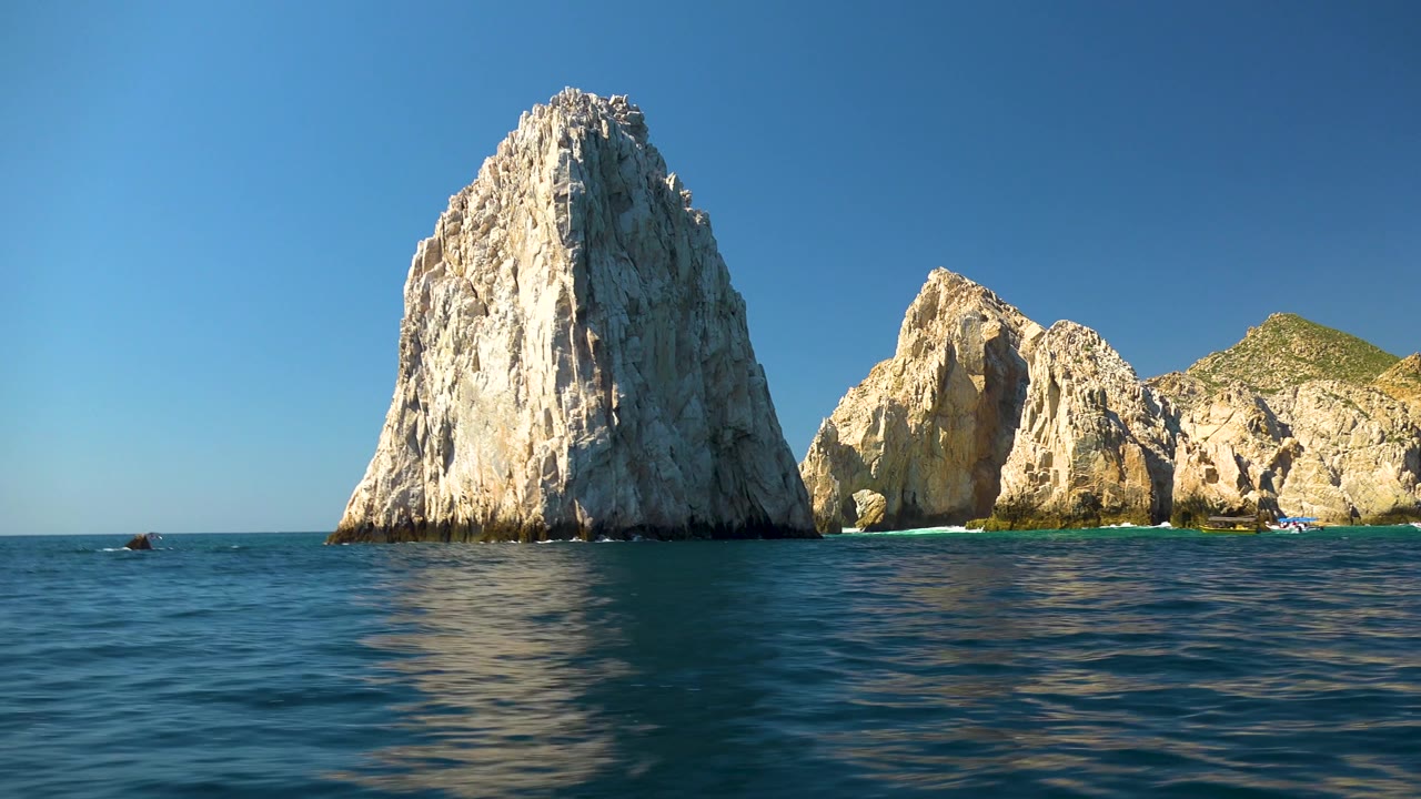 Cabo San Lucas rock formations sit across the horizon with darker ripples and a faint reflection below the tallest rock, with no visible people.