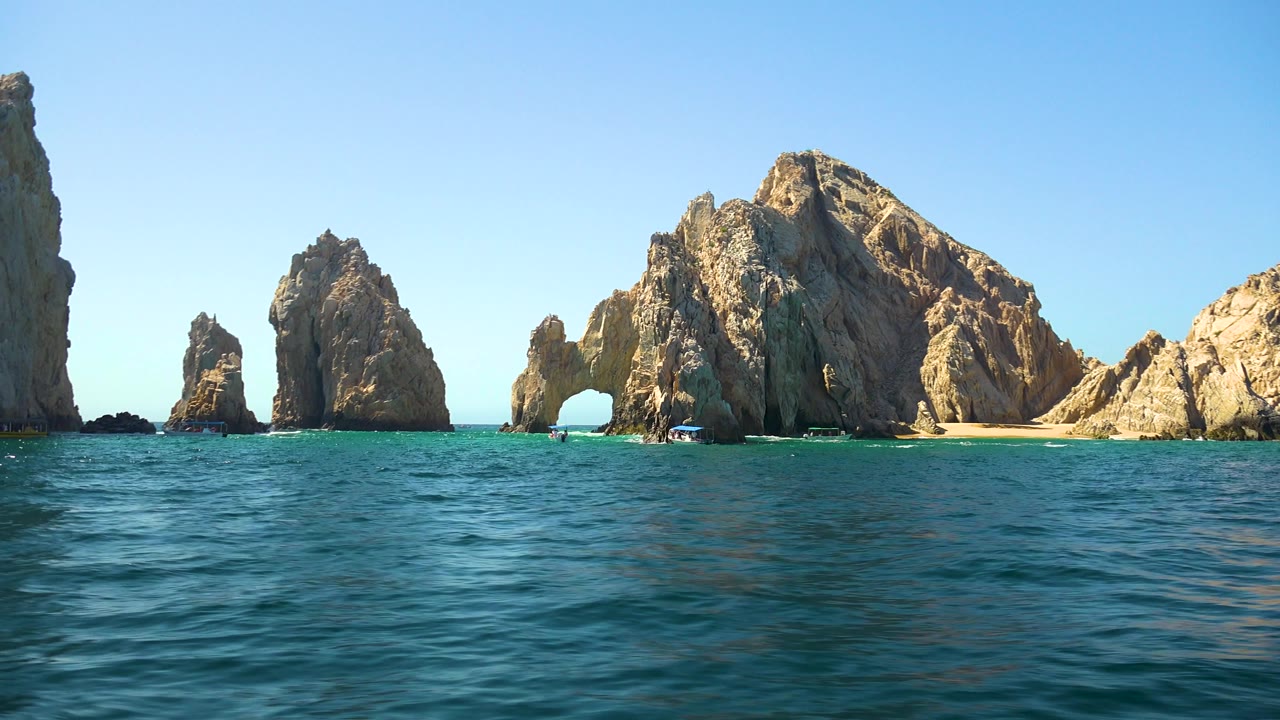 Rock formations and a natural arch seen across blue water.