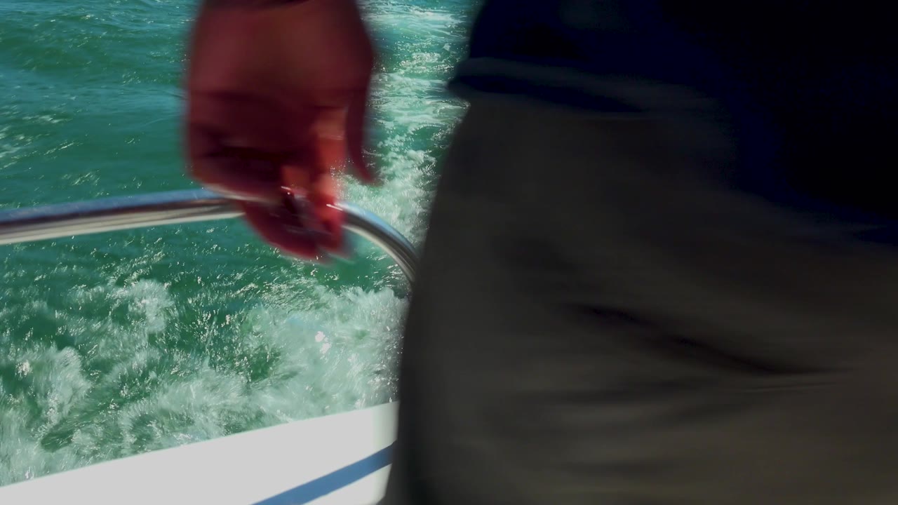 Hand above boat rail with wake behind it