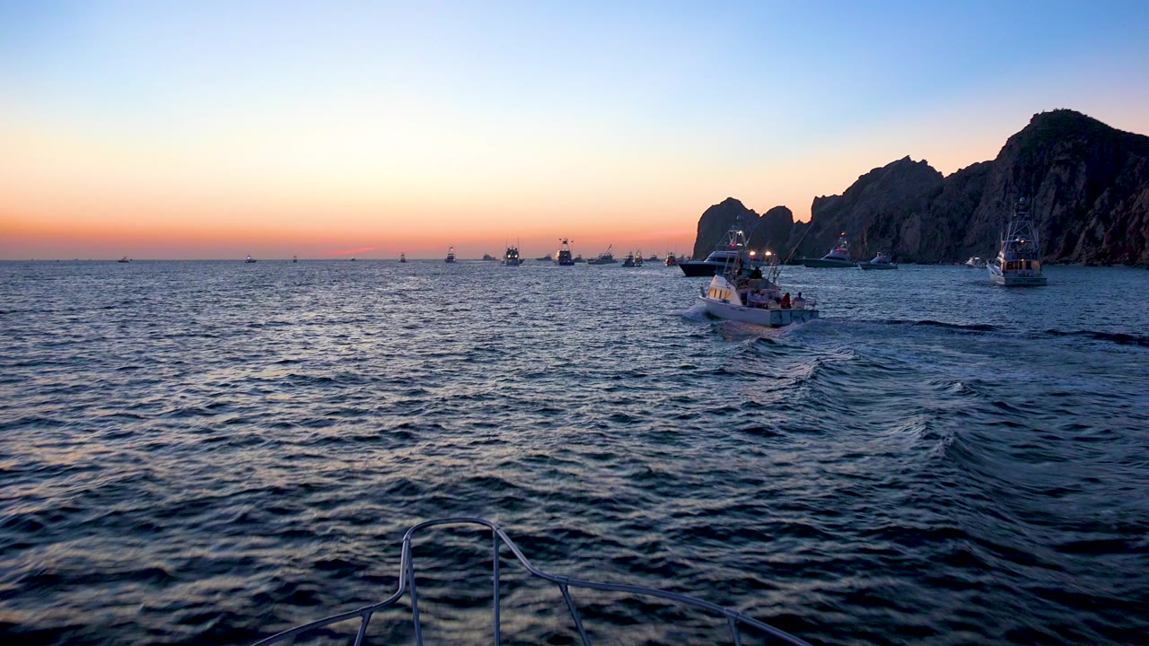 Cabo San Lucas, Mexico water view with a small boat nearer the center, distant boats along the horizon, shadowed cliffs to the right, and no visible people.