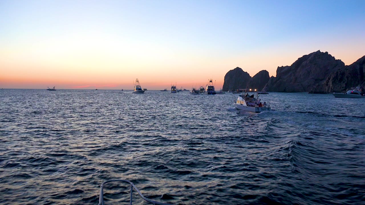 Boat wake leading toward small boats and rocky coast in evening light.
