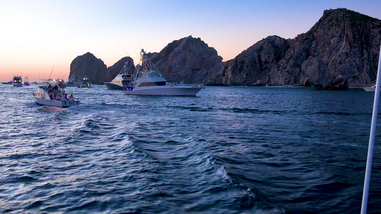 White boats on blue water in front of rocky mountains at sunset.
