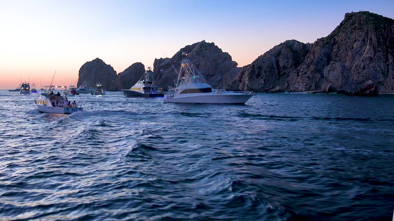 Cabo San Lucas, Mexico frame where a large white boat sits close to the right side of the rock formations, with smaller boats left and no clearly visible people.