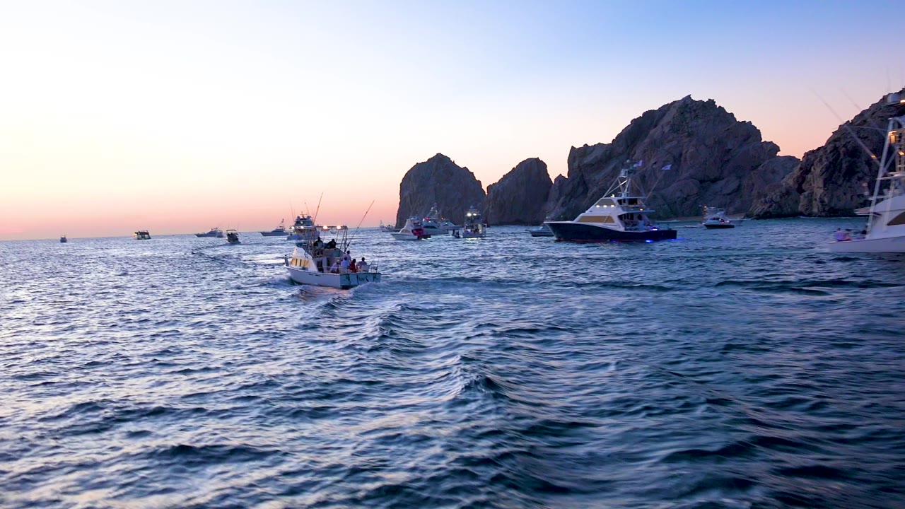 Small boat traveling ahead across blue water with rock formations behind it.
