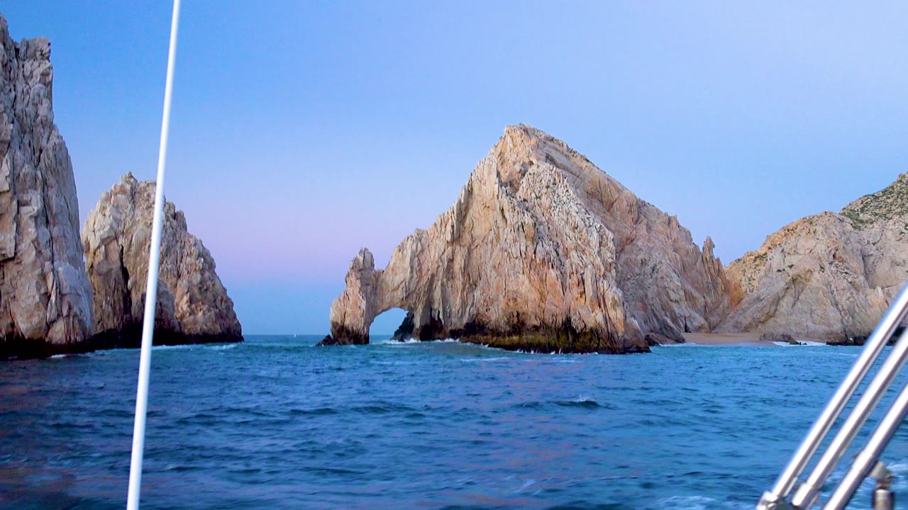 Cabo San Lucas coastal rocks include a tall vertical face at left and an arched opening near the center across blue water, with no visible people.