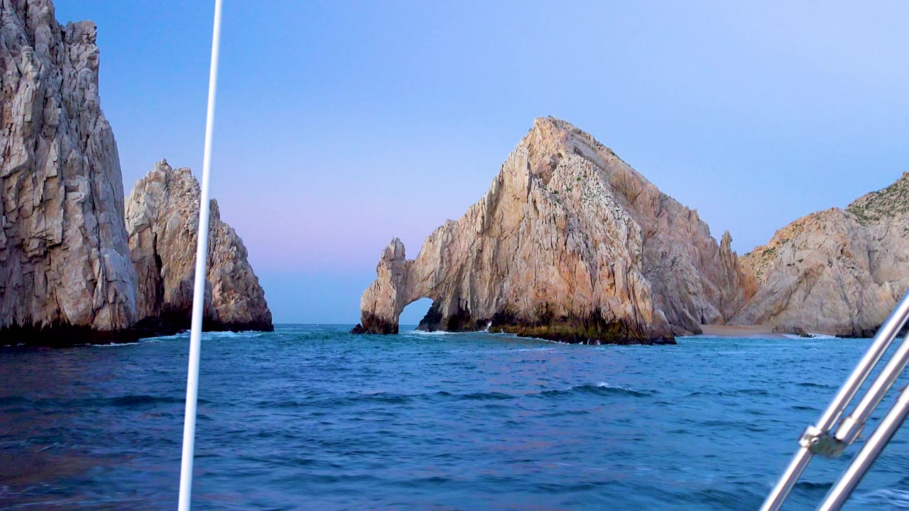 Cabo San Lucas rocks remain centered beyond the blue sea while the white boat pole crosses the left foreground and no visible people appear.