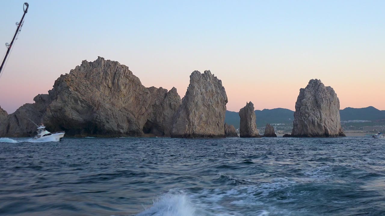 Rock formations in choppy ocean water at sunset with a fishing rod at left.