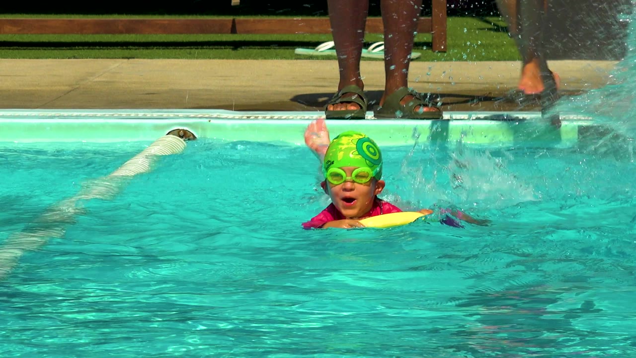 Child in green swim cap swimming beside a lane divider.