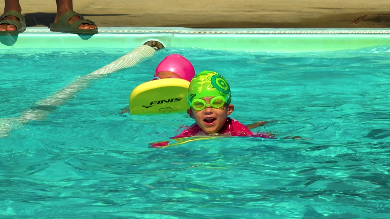 Two children with kickboards face the camera in pool water.