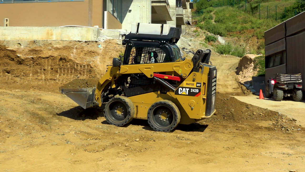 Skid-steer loader crossing a dusty site with bucket raised slightly.
