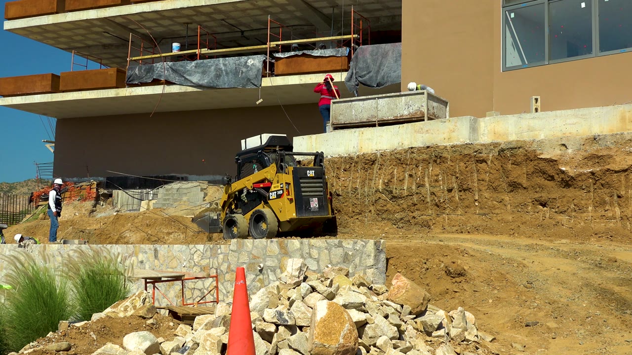 Skid steer beside dirt slope below unfinished building.