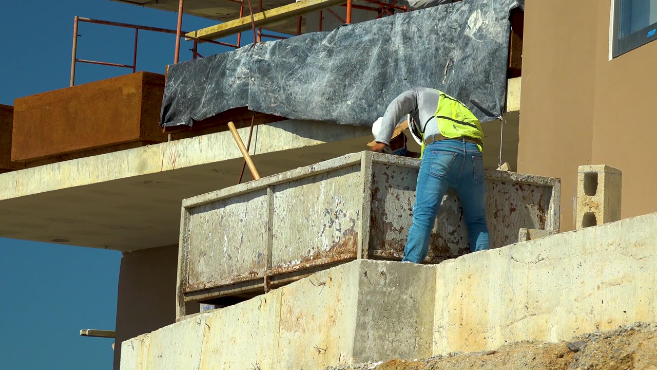 In Cabo San Lucas, the worker shifts toward the right of the frame while working behind the concrete ledge and metal container.