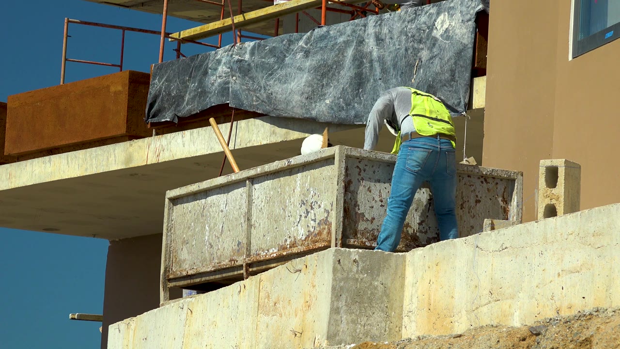 Worker bends behind a rusty container on a concrete platform.