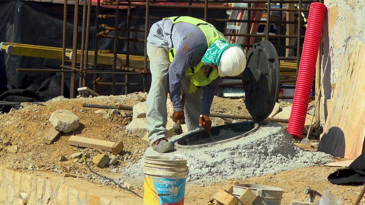 Worker in safety vest hammering near a round concrete opening.