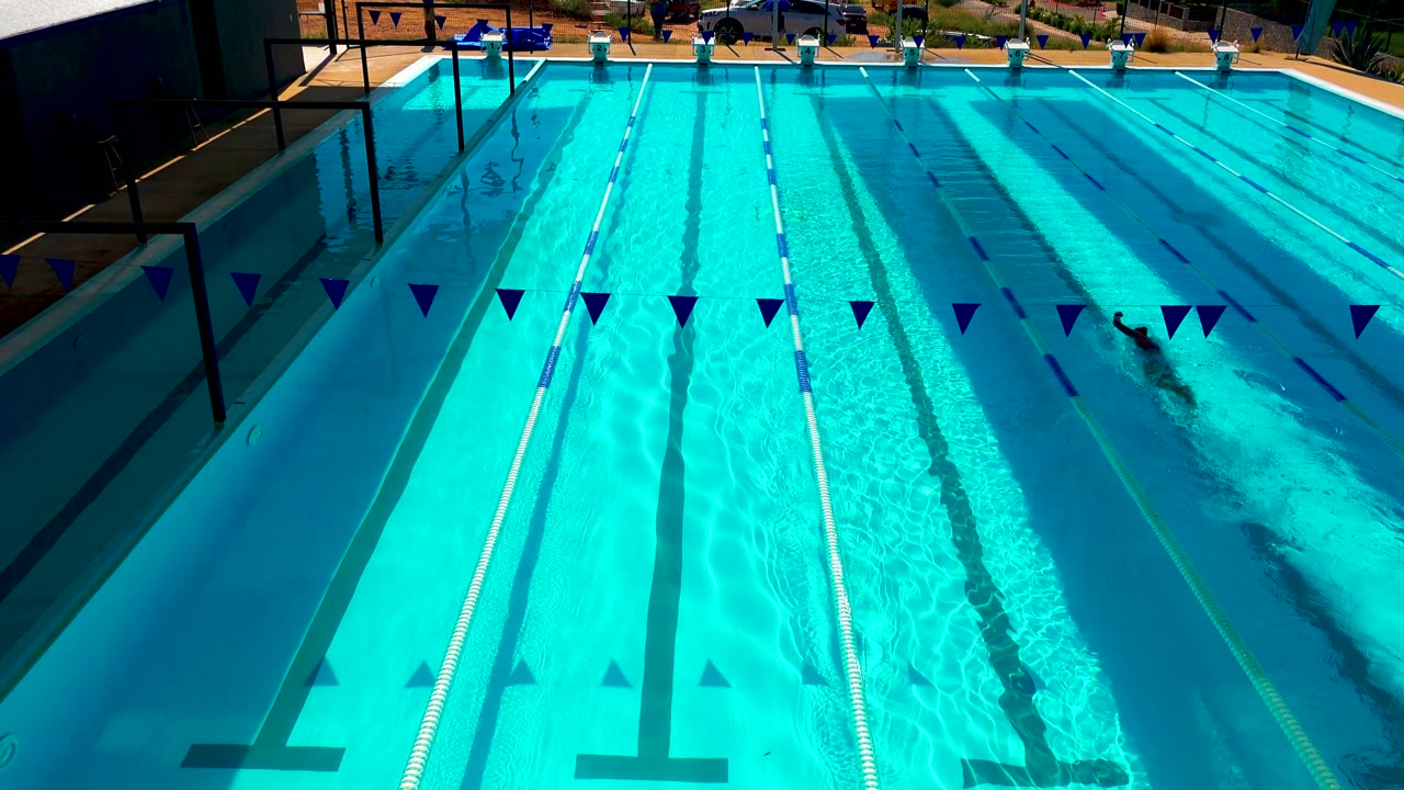 Outdoor lap pool with lane lines, blue flags, and bright water reflections.