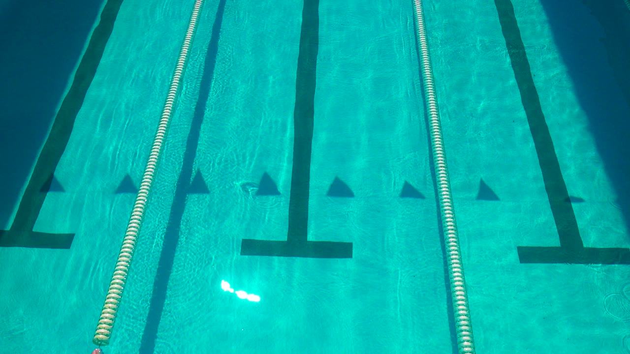 Turquoise pool water in Cabo San Lucas with a floating lane rope near the center-left, black floor lines, triangular distance markers, and no visible people.