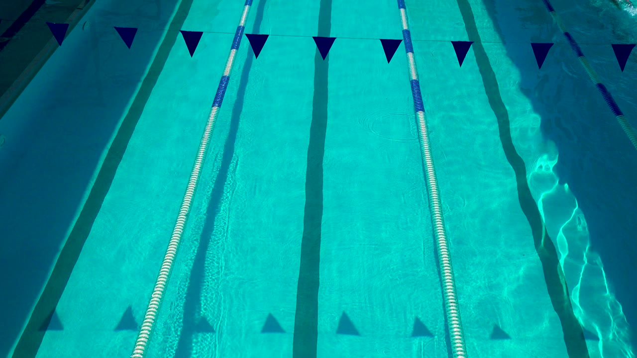 Turquoise swimming pool water in Cabo San Lucas with a white lane rope, dark lane markings, triangular pennant flags, and no visible people.