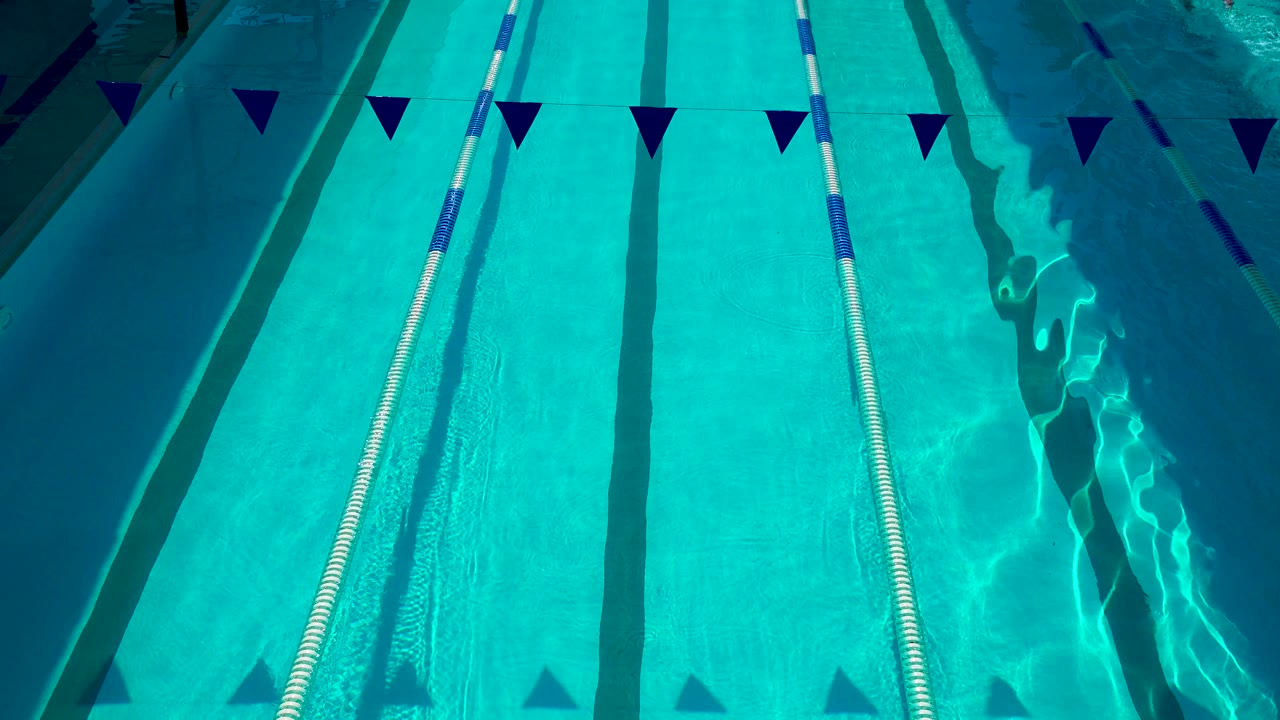 Bright Cabo San Lucas swimming pool frame with pennant flags, a vertical lane rope, dark lane stripes, and brighter rippled water along the right side with no visible people.