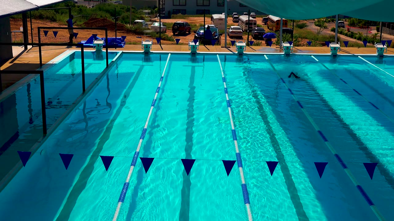 Sunlit pool lanes with foreground flags and a swimmer near the right side.