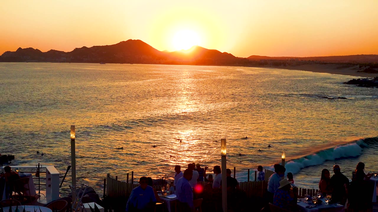 Sunlit sea and mountain horizon seen from a terrace with people in shadow.