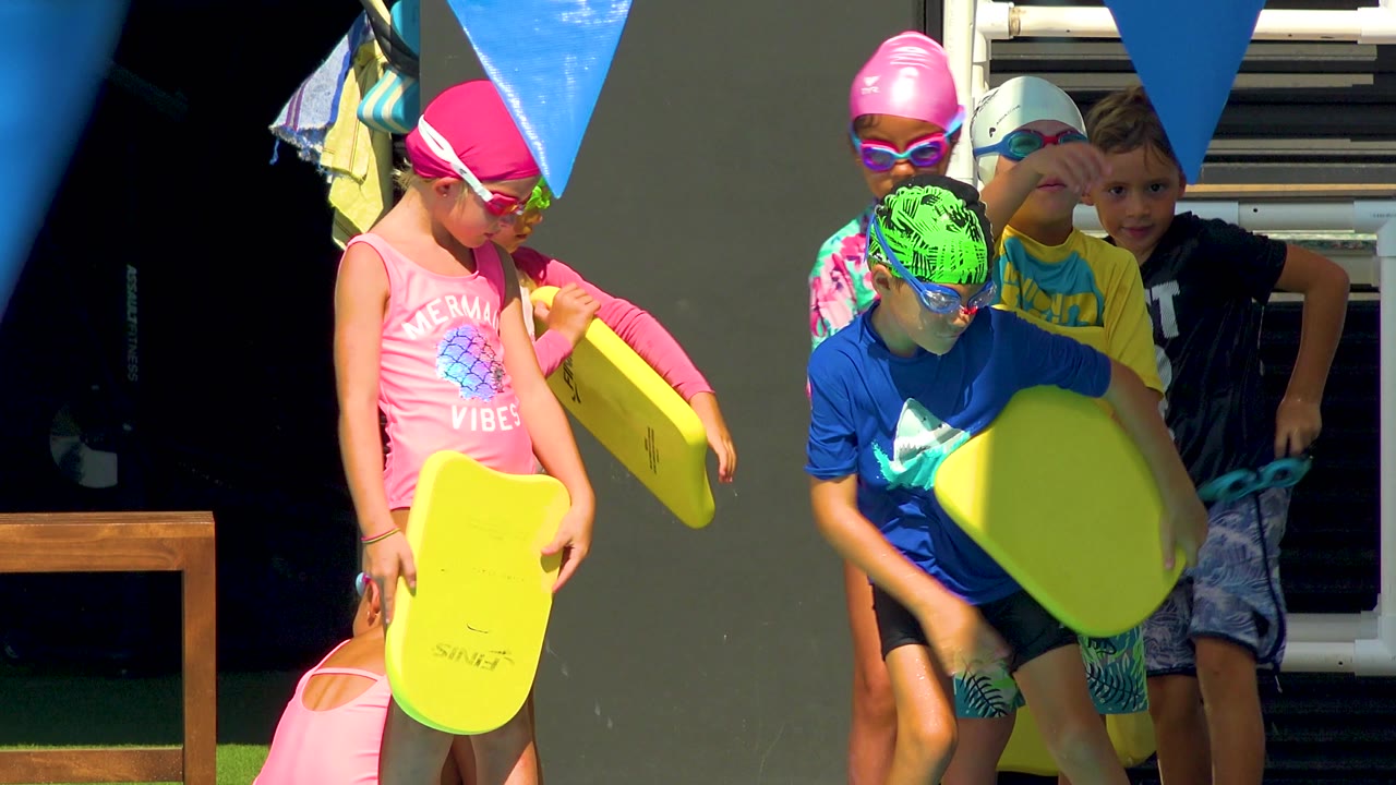 Children stand close together holding kickboards beside the pool.