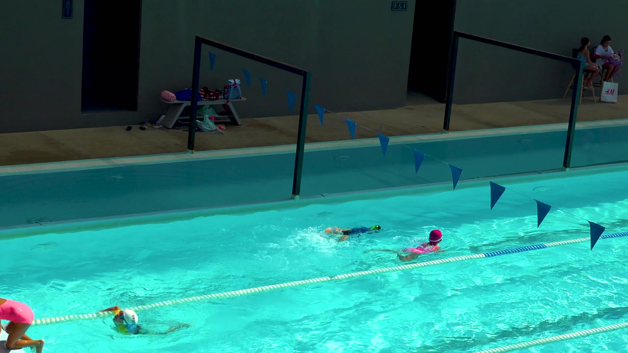At 0:02 in Cabo San Lucas, Mexico, a child in a bright swim cap moves beside a lane rope while another swimmer advances farther across the pool.