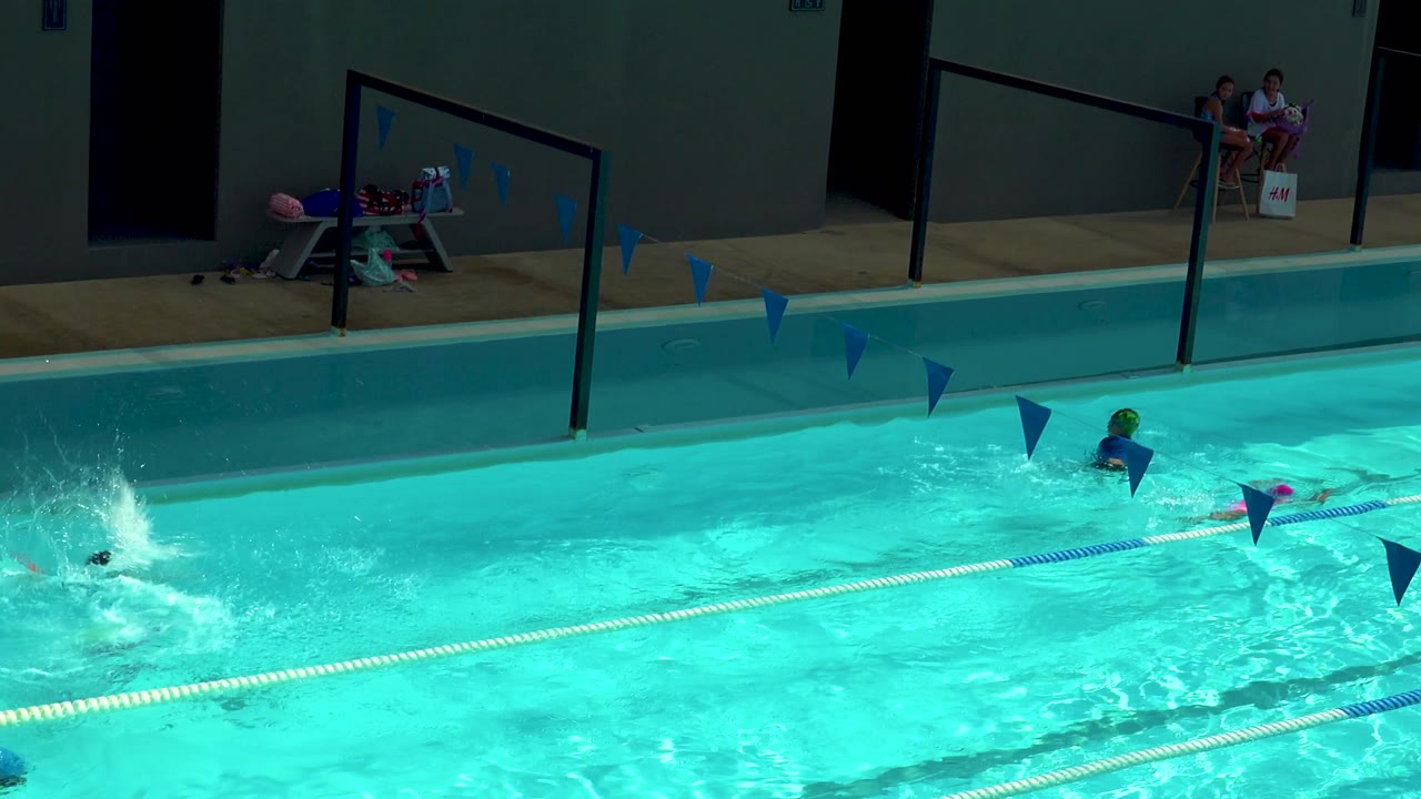 A swimmer splashes near the left side of the Cabo San Lucas pool while other children move through lanes marked by floating ropes and blue pennant flags.