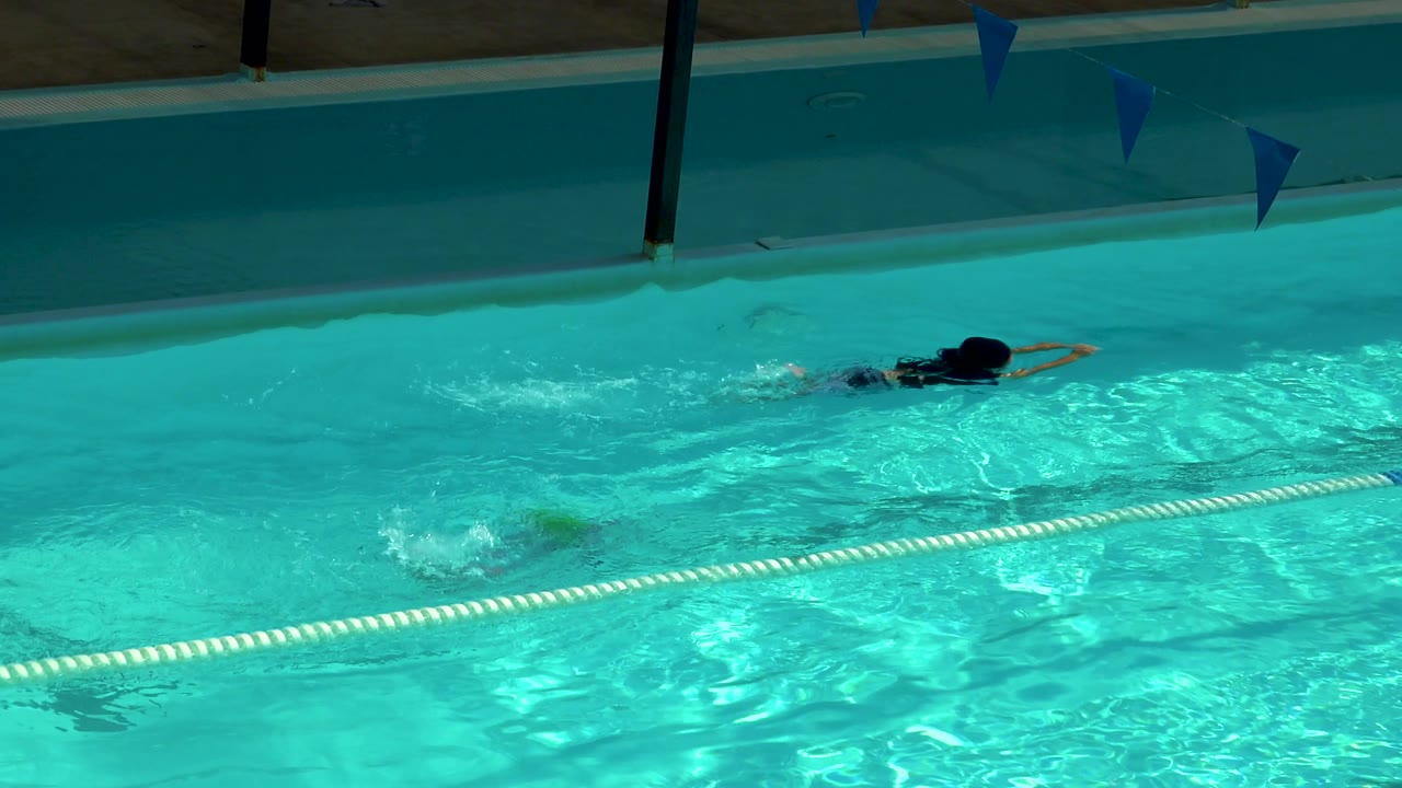 Child remains underwater near the lane rope as another swimmer crosses the pool.