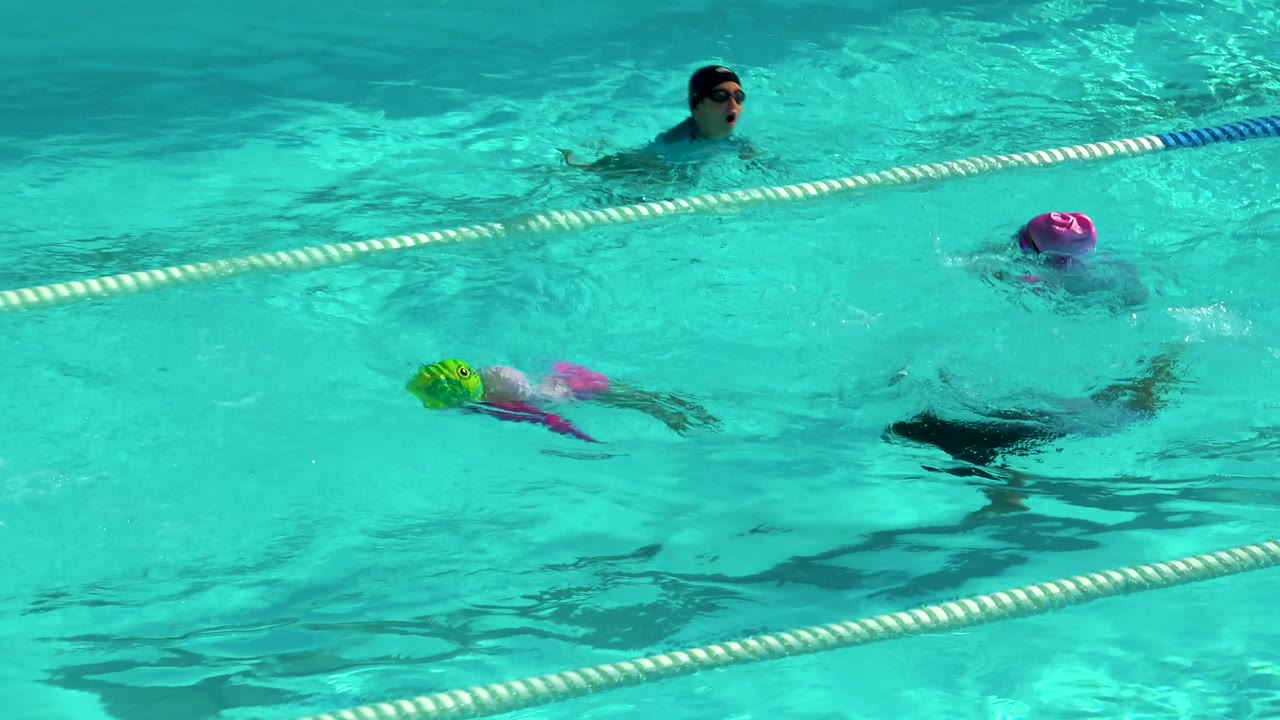 Children in swim caps crossing turquoise pool lanes