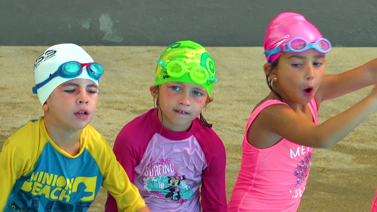 Girl in a pink swim cap reaches forward beside two children.