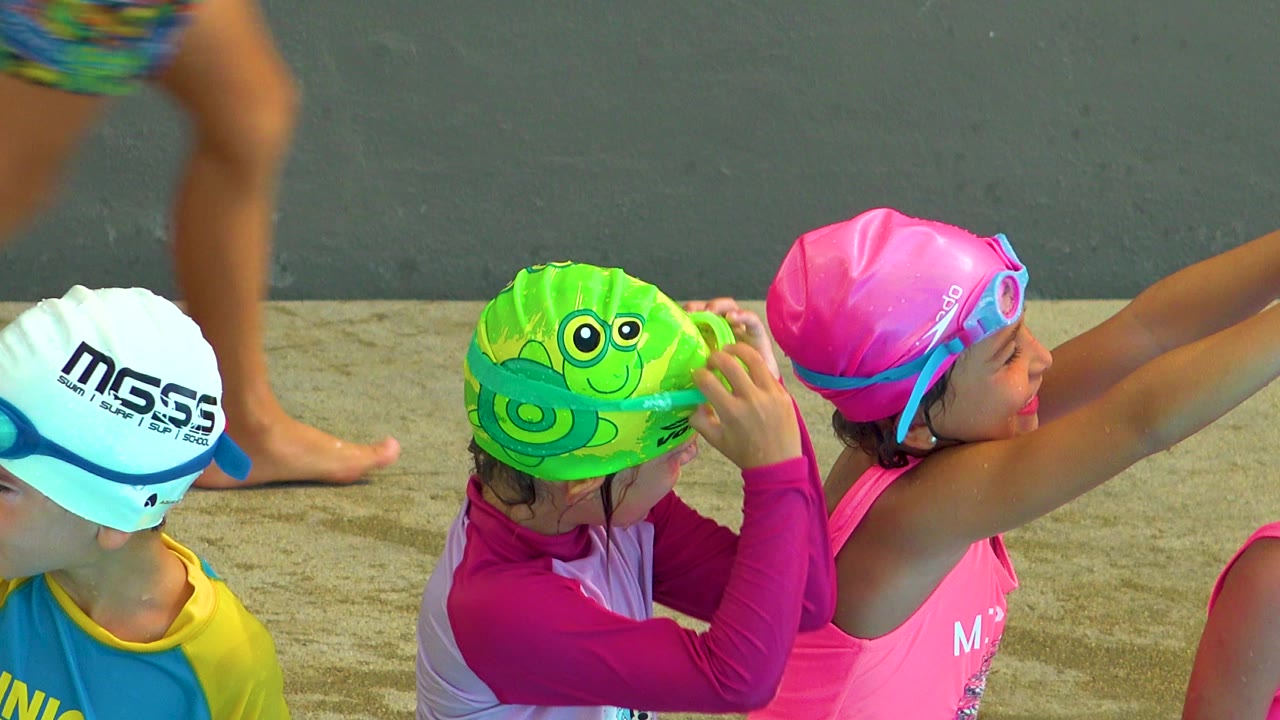 Girl in pink swim cap raises her arms near friends.