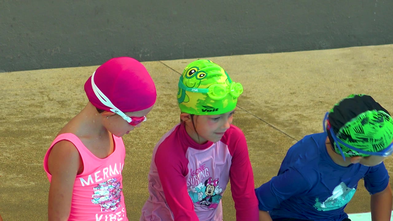 The left and middle children sit in profile at the Cabo San Lucas pool edge while the blue-shirted child on the right is partly cropped near the frame edge.
