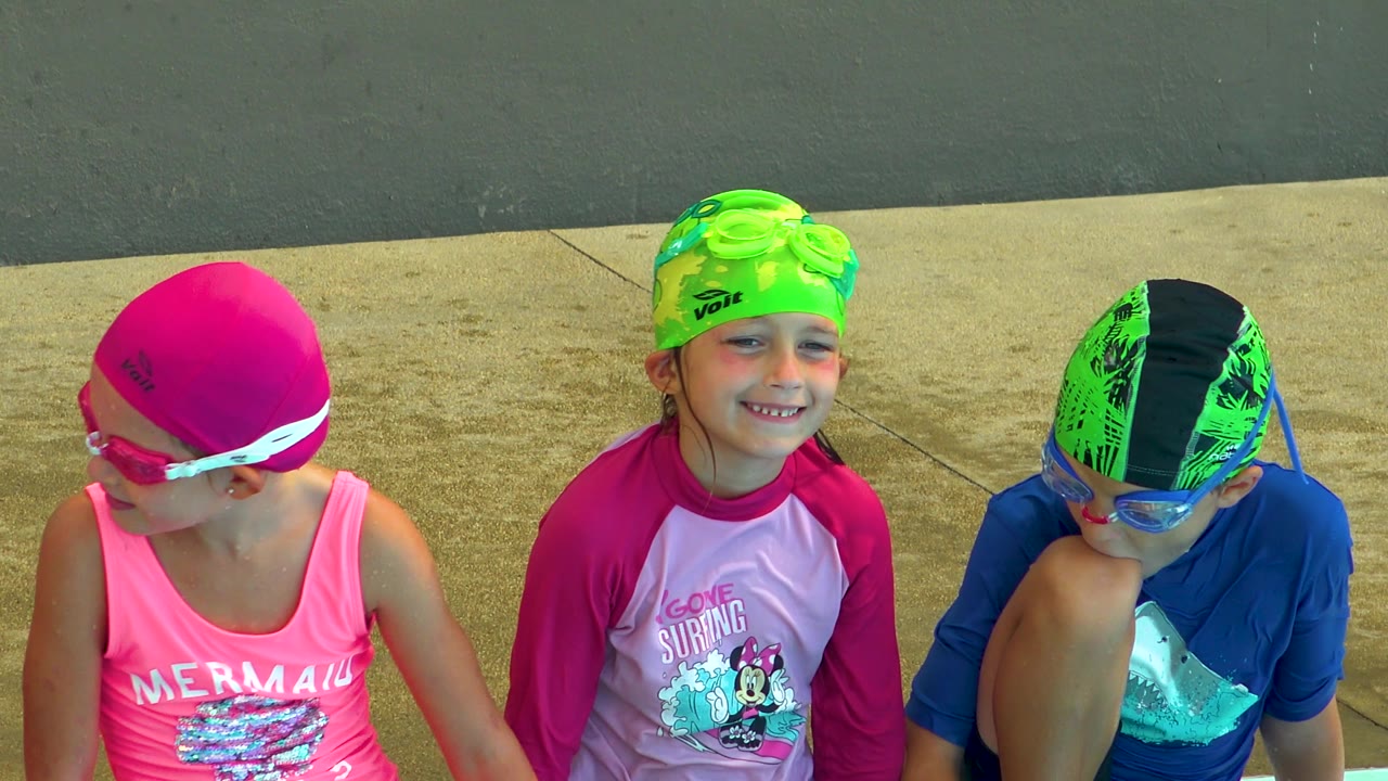 At poolside in Cabo San Lucas, Mexico, the child in the pink cap turns toward the child in the green cap while the child in blue looks downward.