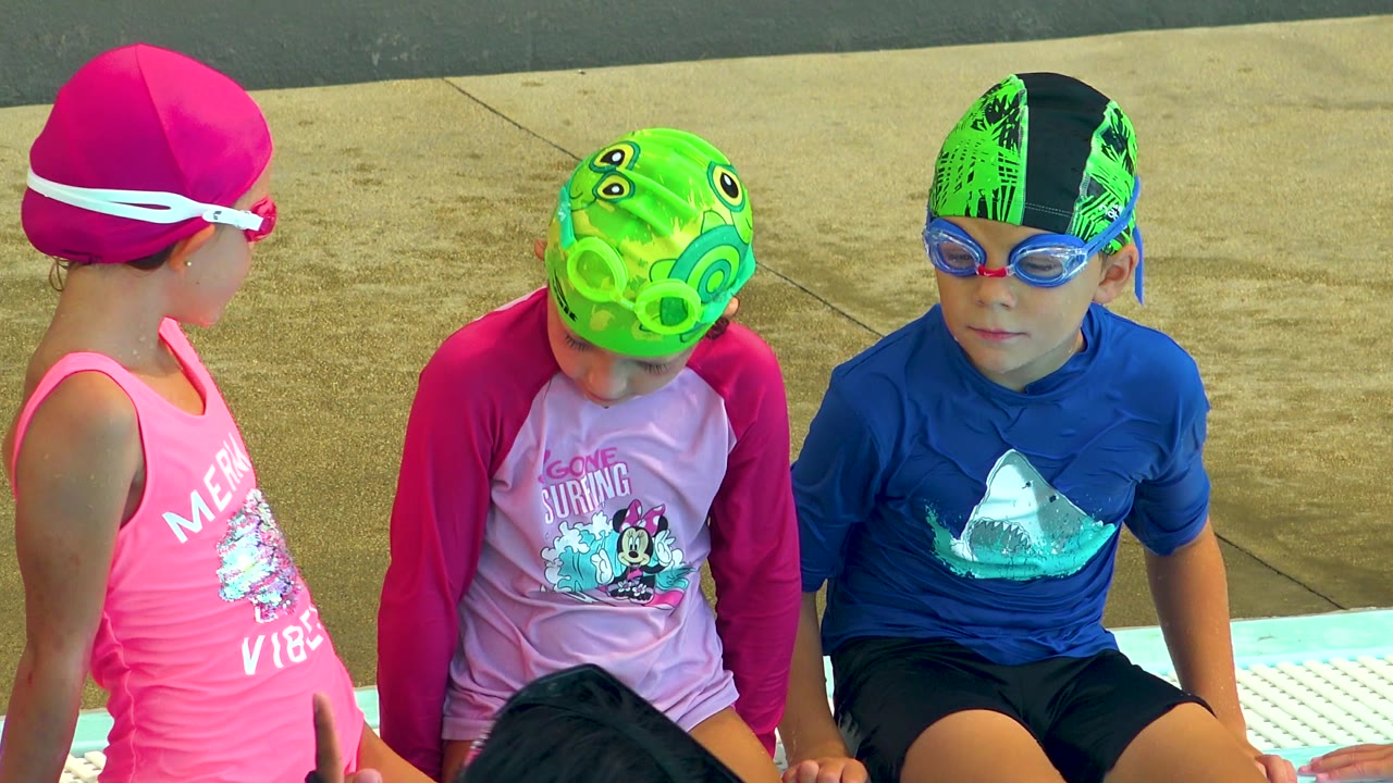 Three children in Cabo San Lucas sit above the pool, with the girl in the pink cap angled away while the center child looks down and the boy in blue faces forward.