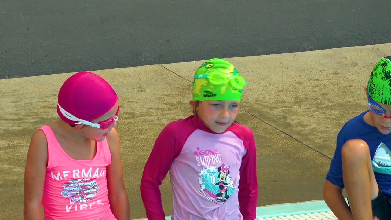 Two children in bright swim caps sit beside a partially visible child.