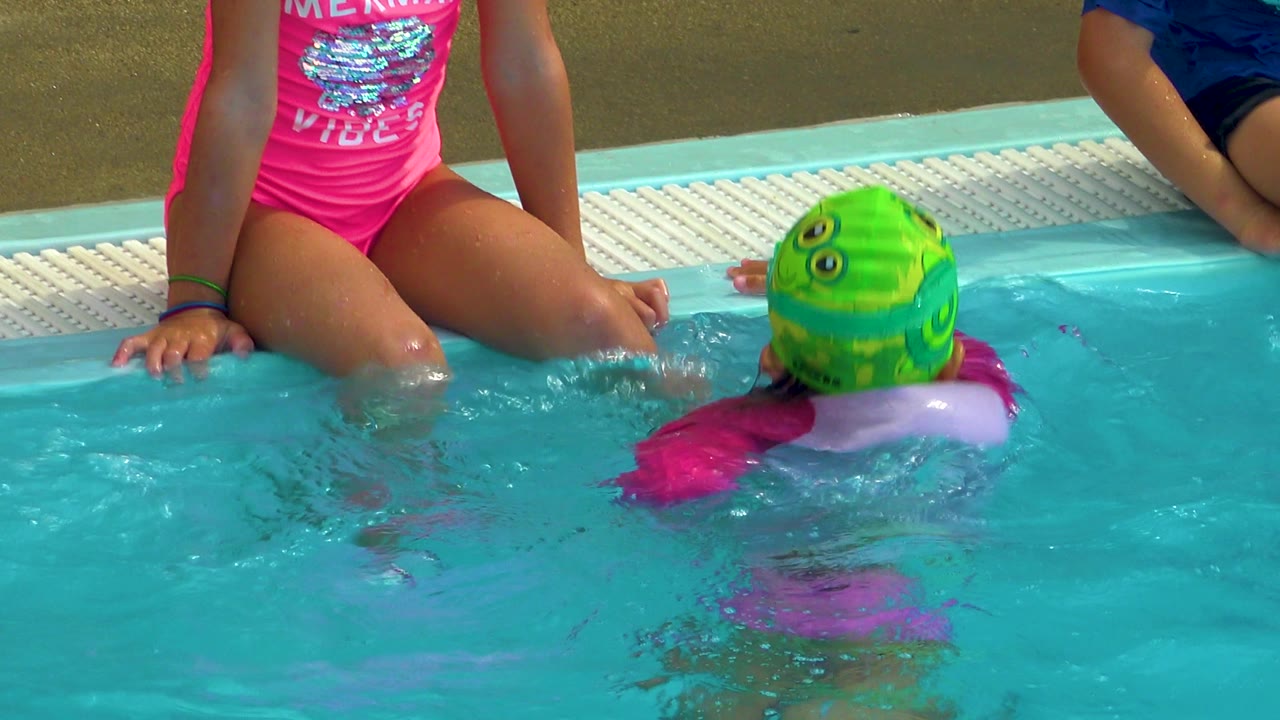 In Cabo San Lucas, Mexico, the child in the green swim cap turns upright in the pool near a seated child in pink, with another child partly visible on the right.