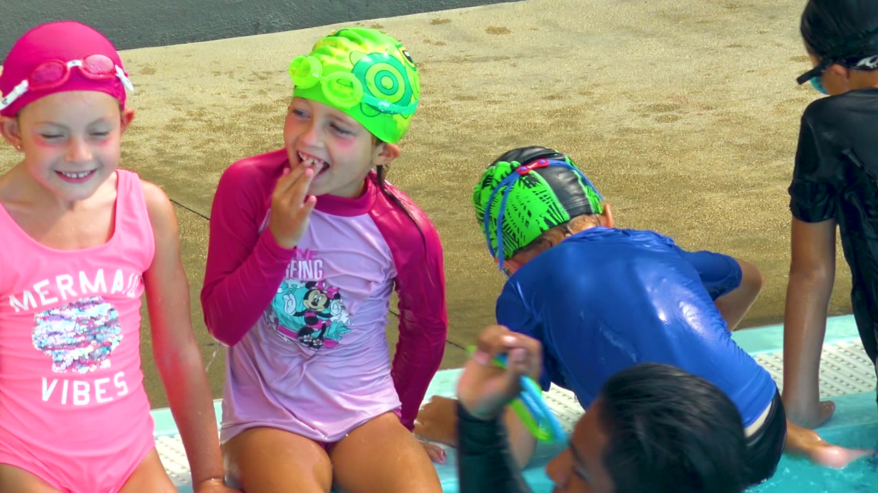 Two girls sit beside other children at a pool edge.
