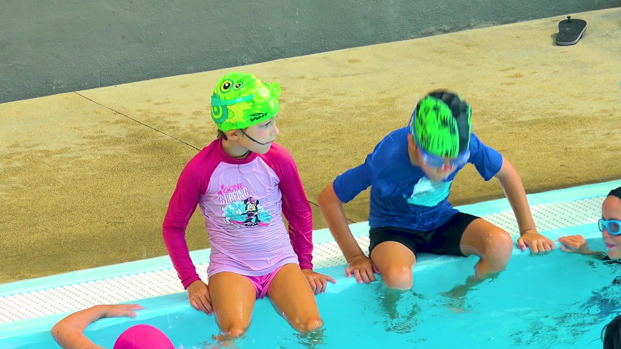 Two children sit at the edge of the pool in Cabo San Lucas, Mexico, while another child in a pink cap is partly visible in the water below them.