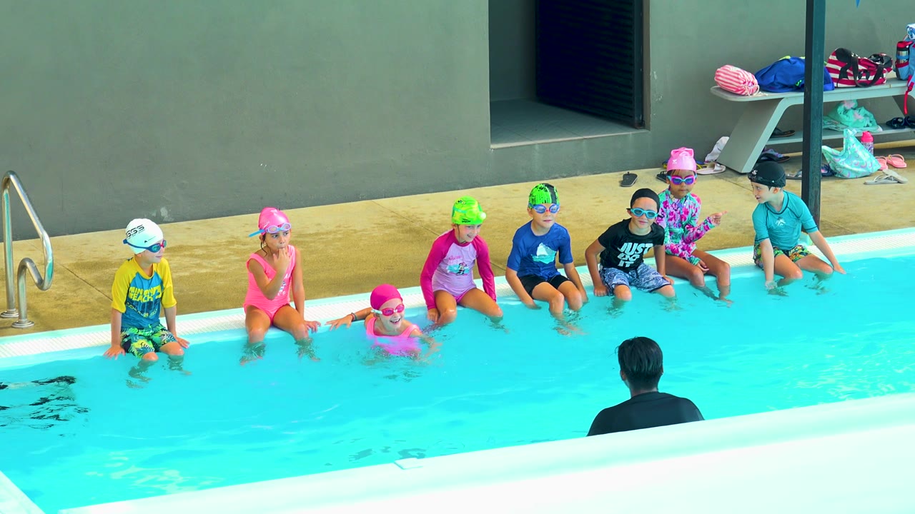 Children remain seated on the pool edge as one child floats near the wall.