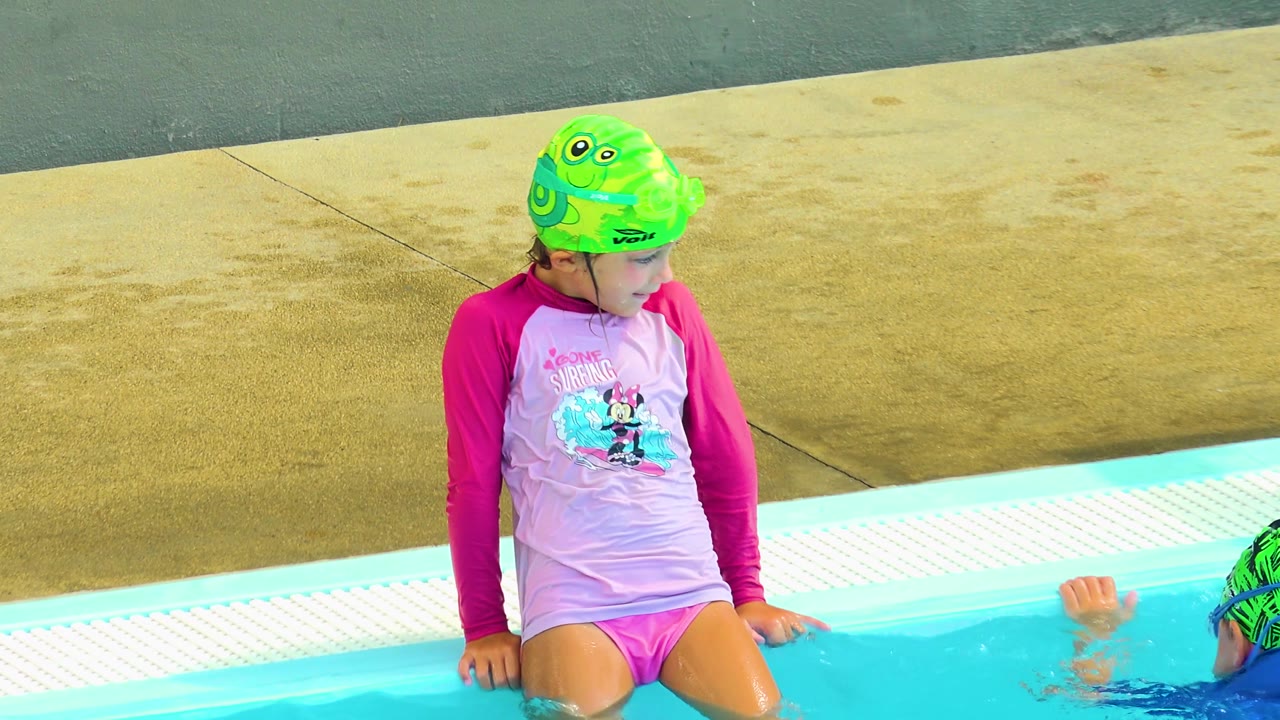 In Cabo San Lucas, Mexico, the child has shifted onto the pool ledge, looking to the side with legs above the water and a partial swimmer at frame edge.